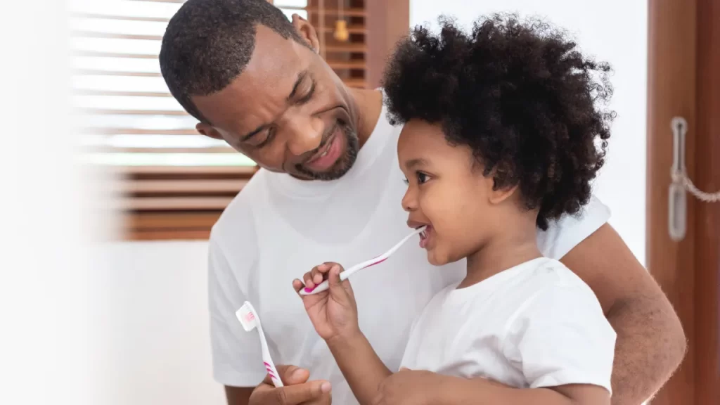 Man showing child how to brush her teeth